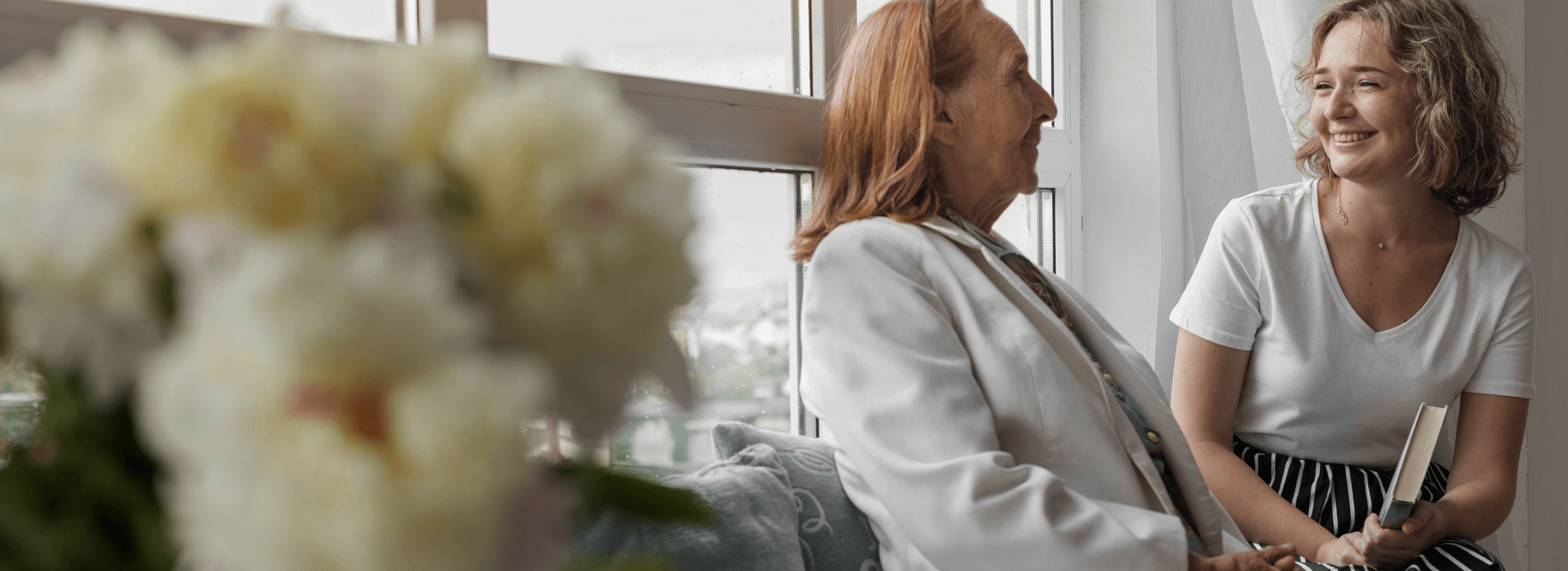 smiling-woman-holding-book-sitting-with-her-granny-window-sill